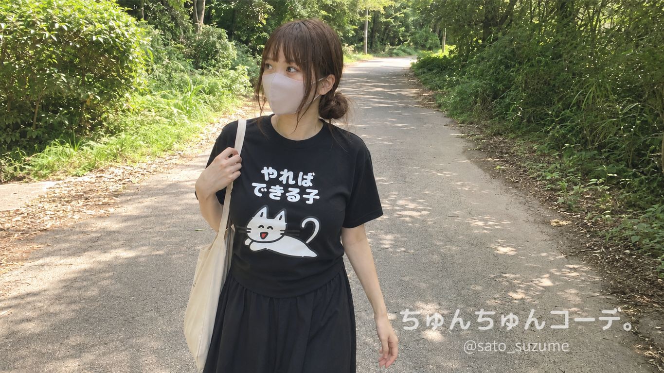「やればできる子」と寝転ぶ猫がプリントされた黒Tシャツを着て田舎道を歩く女性